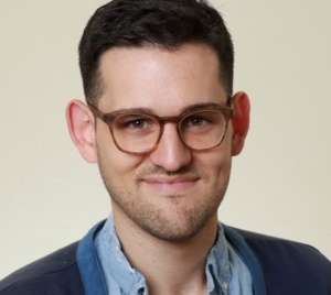 This is a headshot of Lifetime Arts Trainer, Vinny Mraz. He has dark brown hair and brown glasses. He is smiling.