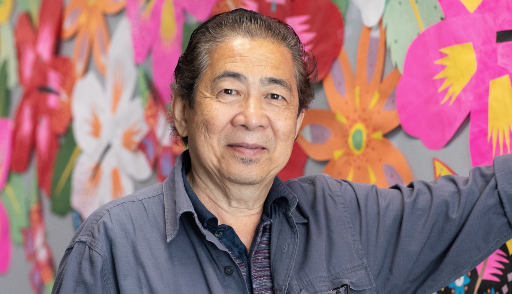 Photo of a man standing in front of a colorful floral mural.