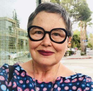 A headshot of Debra Pasquerette. She has short hair and brown eyes with black framed glasses. She is smiling.
