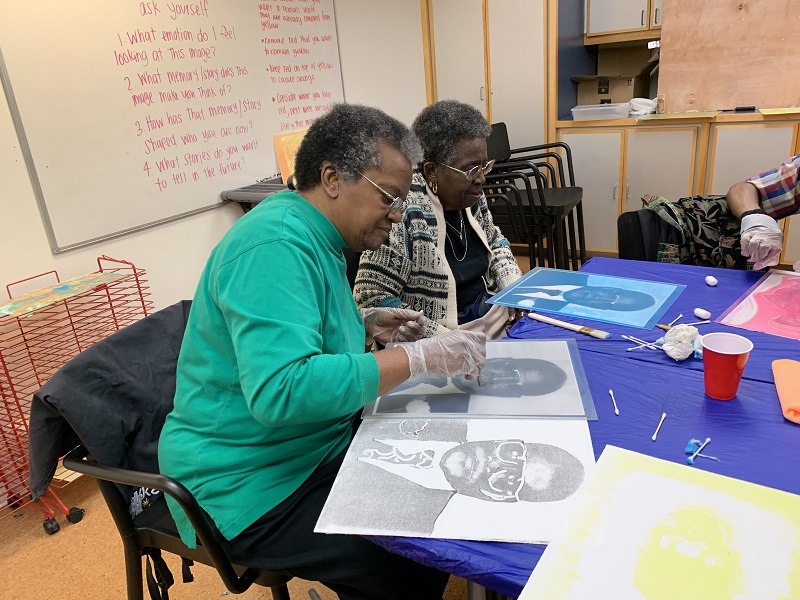 Older adult participants work on their print projects at a table.
