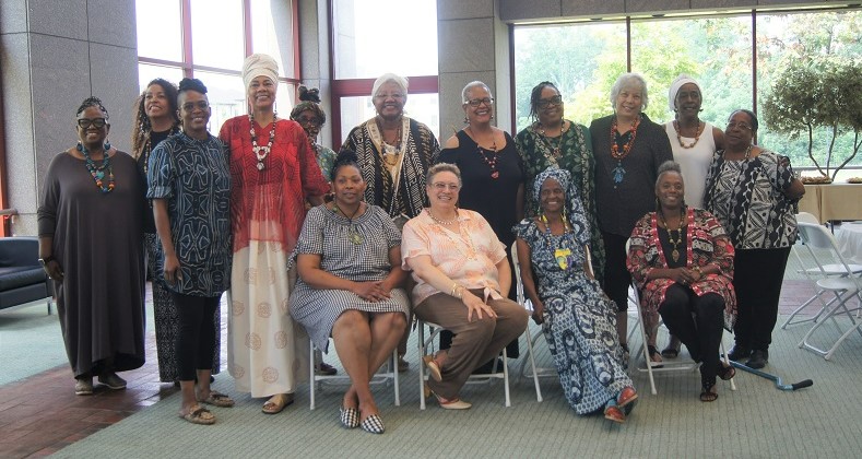 A group of older adult participants smile and pose with teaching artist, Rosa Rojas.
