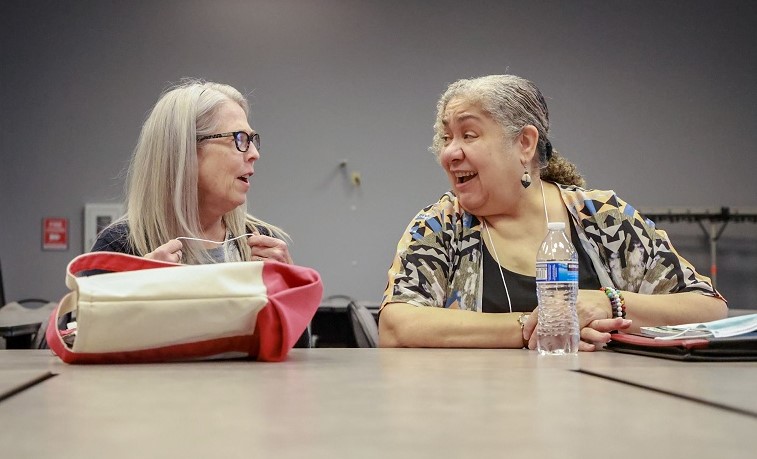 Two teaching artists talking to each other while sitting at a table.